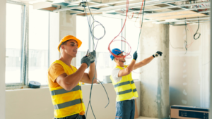Two construction workers performing asbestos abatement in a room with wires.